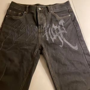 Svarta jeans med broderad text - Snygga svarta jeans från Revenge med unik broderad text på framsidan. De har en klassisk femficksdesign och kontrasterande sömmar. Perfekta för en cool och avslappnad stil. Jag är 180 cm och de passar perfekt. Passar m och s.