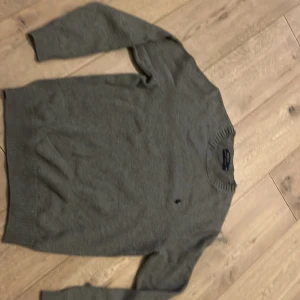 Grå stickad tröja från Polo Ralph Lauren - Säljer en stilren grå stickad tröja från Polo Ralph Lauren. Tröjan har långa ärmar och en ribbad rund halsringning. Perfekt för kyligare dagar och ger en klassisk look.
