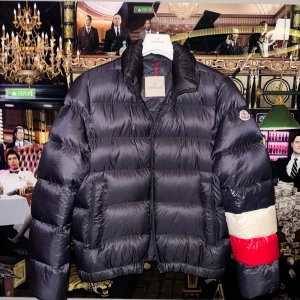Unik pufferjacka från Moncler - Säljer en snygg pufferjacka från Moncler med coola detaljer. Jackan har en dragkedja framtill och långa ärmar med en röd, blå och vit rand på ena ärmen. Perfekt för att hålla värmen under kyliga dagar. Storlek 3 som motsvarar en M/L. Cond: 9/10. Kvitto från Moncler Oslo finns kvar.
