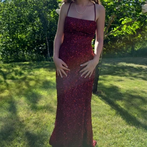 Vinröd balklänning  - Jättefin vinröd balklänning med paljetter och slits (se bild). Endast använd 1 gång, som ny. Klänningen har öppen rygg med superfin justerbar knytning. Klänningen är upplagd av en skräddare. Passar perfekt på mig som är 158cm med klack på 6,5 cm (mätt från insidan av klacken). Klänningen har även axelband som man kan använda till ryggknutningen om man vill ha utan axelband. Kontakta mig först vid intresse eller om du har några frågor 🥰