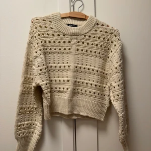 Beige stickad tröja från Gina Tricot - Säljer en beige stickad tröja från Gina Tricot i storlek S. Tröjan har ett hålmönster och är croppad med långa ärmar.