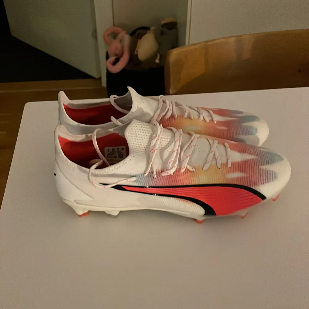 Snygga fotbollsskor från Puma i en mix av vitt, orange och blått med svarta detaljer.. Kengät.