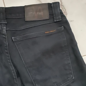 Svarta jeans från Nudie Jeans - Snygga svarta jeans från Nudie Jeans med en klassisk femficksdesign. De har en diskret logga på bakfickan och en läderpatch vid midjan. Perfekta för en stilren look.