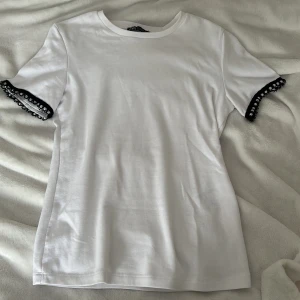 Vit t-shirt med pärldetaljer från Zara - Säljer en superfin vit t-shirt från Zara med pärldetaljer på ärmarna, aldrig använd, hör av er vid frågor💗
