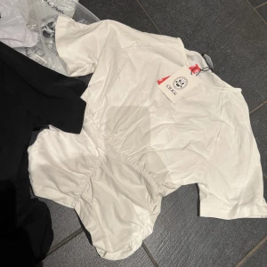 Vit populär kortärmad topp från Cider - Säljer en stilren vit topp från Cider med korta ärmar och en lätt rynkad detalj i midjan. Perfekt för en enkel och elegant look. Toppen är gjord i ett mjukt och bekvämt material. Helt ny med prislapp men tyvärr passa den inte.