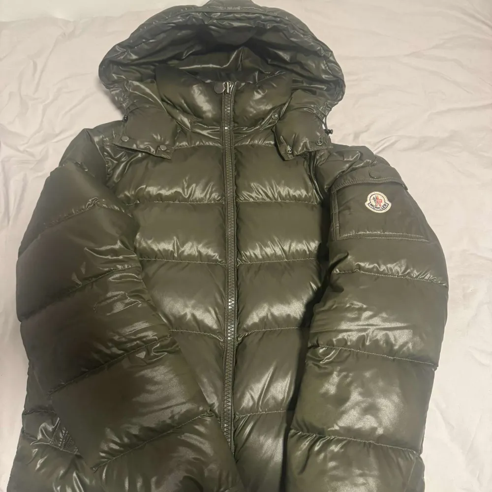 Säljer en snygg grön dunjacka från Moncler med huva och dragkedja. Jackan har ett broderat Moncler-märke på ärmen och knappar vid axlarna. Perfekt för kyliga dagar! Jackan är 9/10 skick.. Takit.