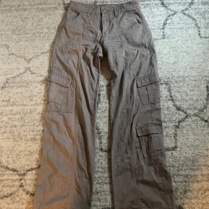 Bruna cargobyxor - Säljer ett par bruna cargobyxor med breda ben och flera praktiska fickor på sidorna. Byxorna har en avslappnad passform och är perfekta för en casual look. De har en knapp och dragkedja framtill.