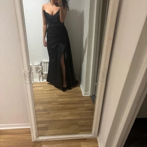 Balklänning  - Elegant svart långklänning med pärldetaljer och draperad överdel. Klänningen har en smickrande slits och smala axelband. Perfekt för bal, helt oanvänd man kan ha den off shoulderen också med band.