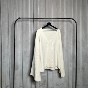 Beige kofta med knappar - Säljer en stilren beige kofta med v-ringning och två dekorativa knappar framtill. Koftan har långa ärmar och en lös passform, perfekt för en avslappnad look.