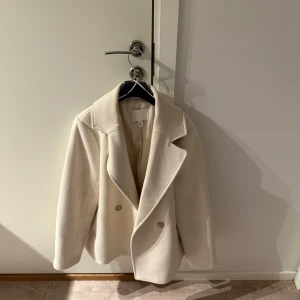 Vit kappa med knappar - Elegant vit kappa med breda slag och dubbelknäppning. Perfekt för kyligare dagar med sin stilrena design. Passar bra till både vardag och mer uppklädda tillfällen. Kappan kommer från HM och är i storlek M💕nypris 499, mitt pris 400