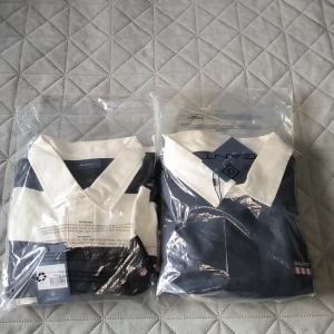 Randig pikétröja från GANT - Säljer en stilren randig pikétröja från GANT i marinblått och vitt. Tröjan har en klassisk krage och knappar framtill. Perfekt för en avslappnad men ändå snygg look. Oanvända ny pris 1500kr! Säljer både 2 endast för 700kr. Storlek M o L.