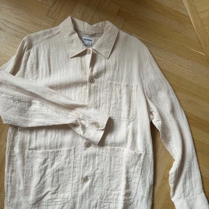 Beige långärmad skjorta från weekday - Snygg beige långärmad skjorta från Weekday i ett lätt och luftigt material. Skjortan har en klassisk krage och knappar framtill. Perfekt för en stilren look.