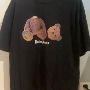 Svart Palm Angels T-shirt - Snygg svart t-shirt från Palm Angels med ett unikt nalletryck på framsidan. T-shirten har korta ärmar och märkeslogga både fram och bak. Perfekt för en cool och avslappnad stil. Väldigt skön