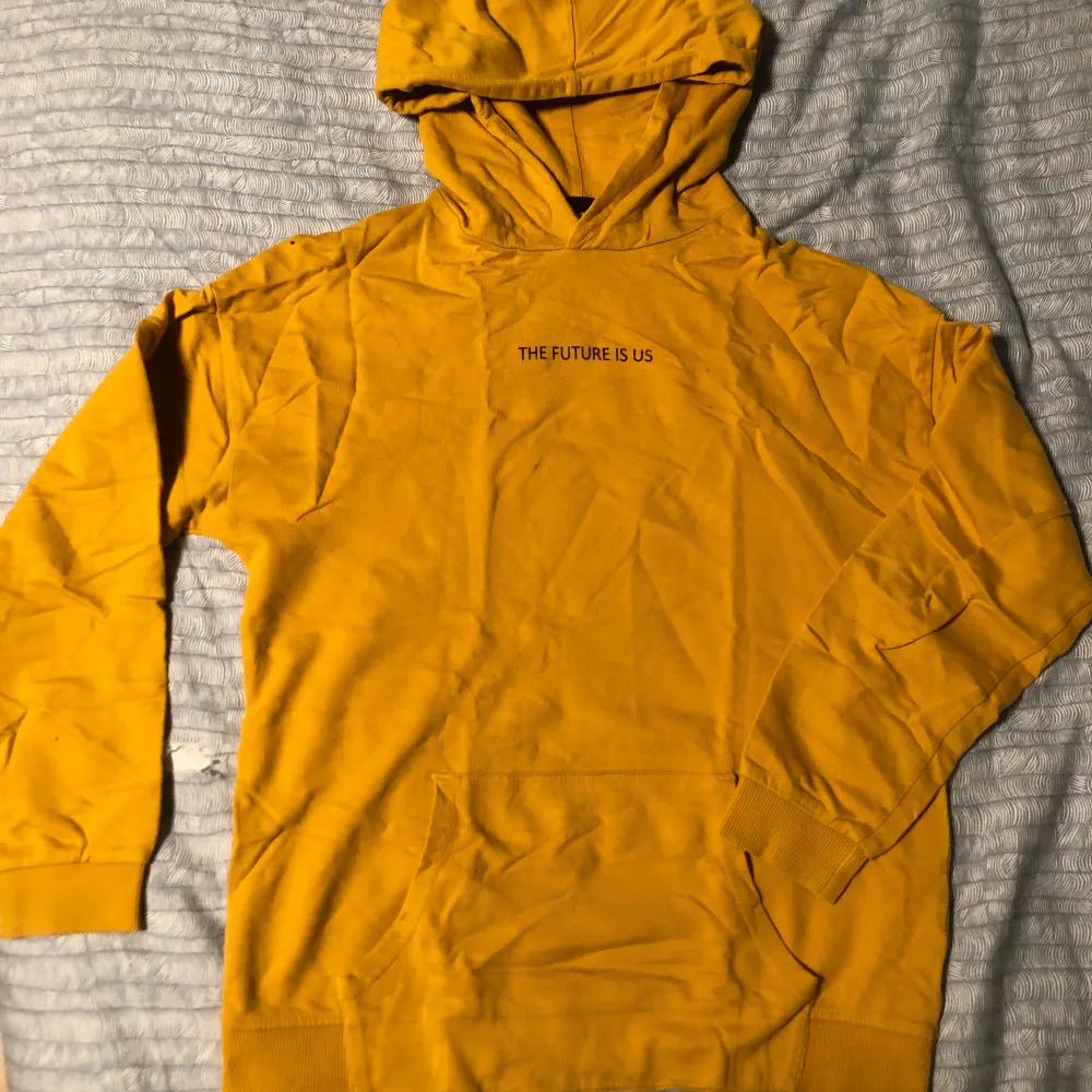 Säljer en gul hoodie från I Love Eco med texten 'THE FUTURE IS US' på bröstet. Tillverkad i ekologisk bomull, perfekt för en bekväm och stilren look. Hoodien har långa ärmar och en klassisk känguruficka framtill.. Neuletakit & Villapaidat.