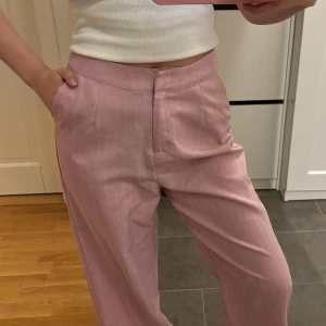 Rosa randiga byxor - Oanvända, rosa lösa luftiga kostymbyxor med vita tunna ränder. Perfekt sommarbyxa.  NLY trend, storlek 34.  Rensar ut endel byxor som jag tänkt sy upp men som aldrig blir av - där av är de helt oanvända. Jag är 160 cm och de är för långa för mig.   💌