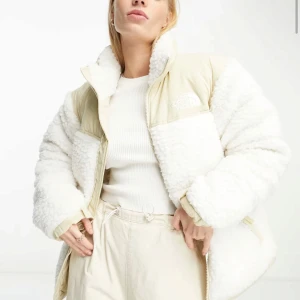 Vit teddyjacka från The North Face - Säljer en mysig vit teddyjacka från The North Face. Jackan har en pufferdesign med dragkedja och hög krage samt Teddymaterial. Passformen är oversized och passar både till dam och herr. Jackan är använd under en vinter, dvs 2-3 månader och har några fläckar (se bilder). Fläckarna går förmodligen bort med mirakelsvamp men jag har inte försökt.          Nypris 4595kr
