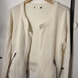 Vit stickad kofta med dragkedjor - Säljer en stilren vit stickad kofta med dragkedjor vid fickorna. Koftan har långa ärmar och en öppen design utan knappar. Perfekt för lager-på-lager under kyligare dagar.