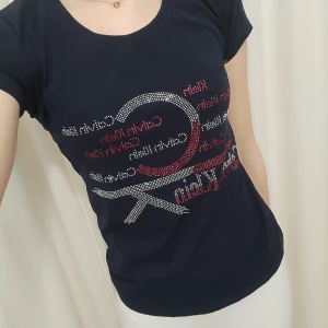 T-shirt med tryck från Calvin Klein - Snygg mörkblå t-shirt från Calvin Klein med ett coolt tryck i rött och vitt på framsidan. Perfekt för en casual look. 