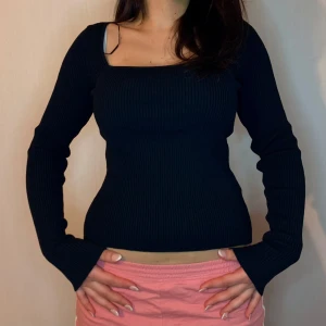 Svart ribbad topp - Snygg svart ribbad topp med långärmad design och fyrkantig halsringning. Perfekt för en stilren look.