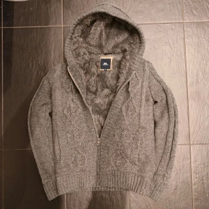 Pälsfodrad cardigan  - Säljer en mysig pälsfodrad cardiganjacka. Väldigt varm och fint kabel stickad. Stilren design med grå päls på insidan och snören. Skriv vid minsta fundering!