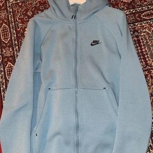 Ljusblå hoodie från Nike - Säljer en ljusblå hoodie från Nike med dragkedja och huva. Den har långa ärmar och en enkel design med Nike-logga på bröstet. Perfekt för en avslappnad stil. Den är slut såld över allt pris 2200kr storlek M hör av er vid intressade.