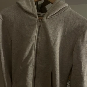 Grå hoodie med dragkedja - Säljer en stilren grå hoodie med dragkedja framtill. Perfekt för en avslappnad look. Den har en bekväm passform och en praktisk huva.