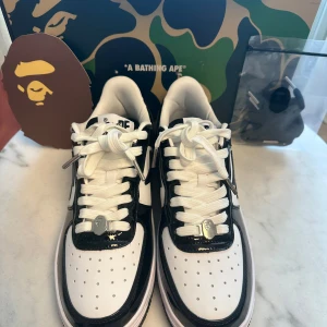 BAPESTA black-white  - Helt nya Bapesta svart i storlek 42.5. Sko med en unik design som kombinerar BAPE:s ikoniska camo-mönster med Nikes klassiska Air Force 1. Skon har en svart glansig läderöverdel med vita detaljer. Skon levereras med original paket och tillbehör.