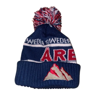 Åremössa - Eftertraktad åremössa. Perfekt för kalla dagar med sin stickade design och ribbad kant. Färgerna är blå, röd och vit vilket ger en sportig look.