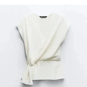 Vit omlottopp från Zara - Elegant vit omlottopp från Zara med knytning i sidan. Toppen har en stilren design och är ärmlös, vilket gör den perfekt för varmare dagar. Passar bra till både jeans och kjol.
