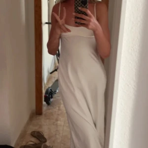 Vit långklänning med öppen rygg - Säljer en elegant vit långklänning med smala axelband och en stilren design. Klänningen har en vacker öppen rygg och är perfekt för somriga tillfällen. Den är tillverkad i ett mjukt och följsamt material som ger en skön passform.