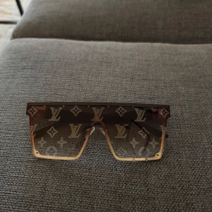 Bruna solglasögon  - Snygga bruna solglasögon . De har en bred, rak design med guldiga detaljer på sidorna. Perfekta för en stilren look.