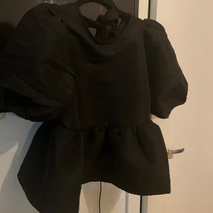 Svart blus med puffärmar - Snygg svart blus från Carin Wester (Åhléns)  med puffiga ärmar och knytning i ryggen. Perfekt för en stilren look. Materialet har en lätt textur som ger en extra dimension till outfiten. Oanvänd  pga för liten. Skriv om du vill ha fler bilder, priset kan diskuteras vid snabb affär. Nypris 599kr