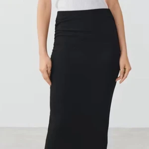 Svart långkjol - Elegant svart långkjol med en tight passform. Kjolen har en stilren design med rynkade detaljer på sidan som ger en smickrande siluett. Perfekt för en chic och sofistikerad look.