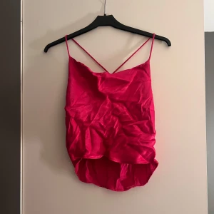 Rosa ärmlös topp - Snygg rosa ärmlös topp med tunna axelband och draperad design. Perfekt för en kväll ute eller en speciell tillställning. Toppen har en lös passform och är tillverkad i ett glansigt material som ger en lyxig känsla.