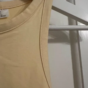 Gul ärmlös klänning - Säljer en stilren gul ärmlös klänning i bomull. Perfekt för varma dagar med sin enkla och bekväma design. Klänningen har en öppen rygg som ger en luftig känsla. Passar utmärkt för en avslappnad look.
