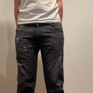 Svarta jeansbyxor från Replay - Snygga svarta jeansbyxor från Replay med slitna detaljer för en cool look. De har en slim passform och är perfekta för en avslappnad stil. Byxorna har klassiska fem fickor och en dragkedja.   Superbra skick