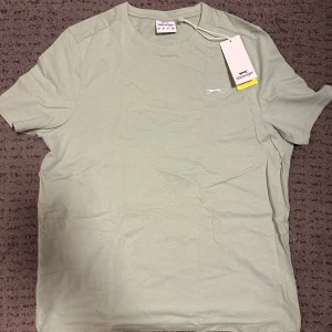 Ljusgrön t-shirt från Slazenger - Säljer en ljusgrön t-shirt från Slazenger. Den har en enkel design med en liten logga på bröstet. Perfekt för en avslappnad stil. T-shirten är kortärmad och gjord i bomull för en bekväm känsla.Ingen frakt utan avhämtning i Göteborg eller Mölndal!