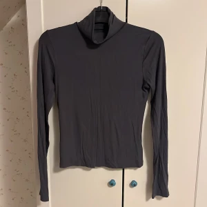 Grå polotröja från BikBok - Säljer en stilren grå polotröja från BikBok. Tröjan har långa ärmar och en klassisk polokrage, perfekt för kyligare dagar. Den är tillverkad i ett mjukt och bekvämt material som ger en skön passform.