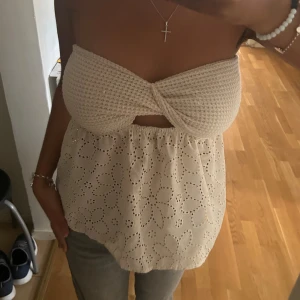 Beige axelbandslös topp med spetsdetaljer - Säljer en superfin beige axelbandslös topp i storlek S. Bekväm och stretchig. Toppen har en twistad design vid bysten och är dekorerad med vackra spetsdetaljer i ett blommönster. Perfekt för sommaren och festliga tillfällen! 🌸