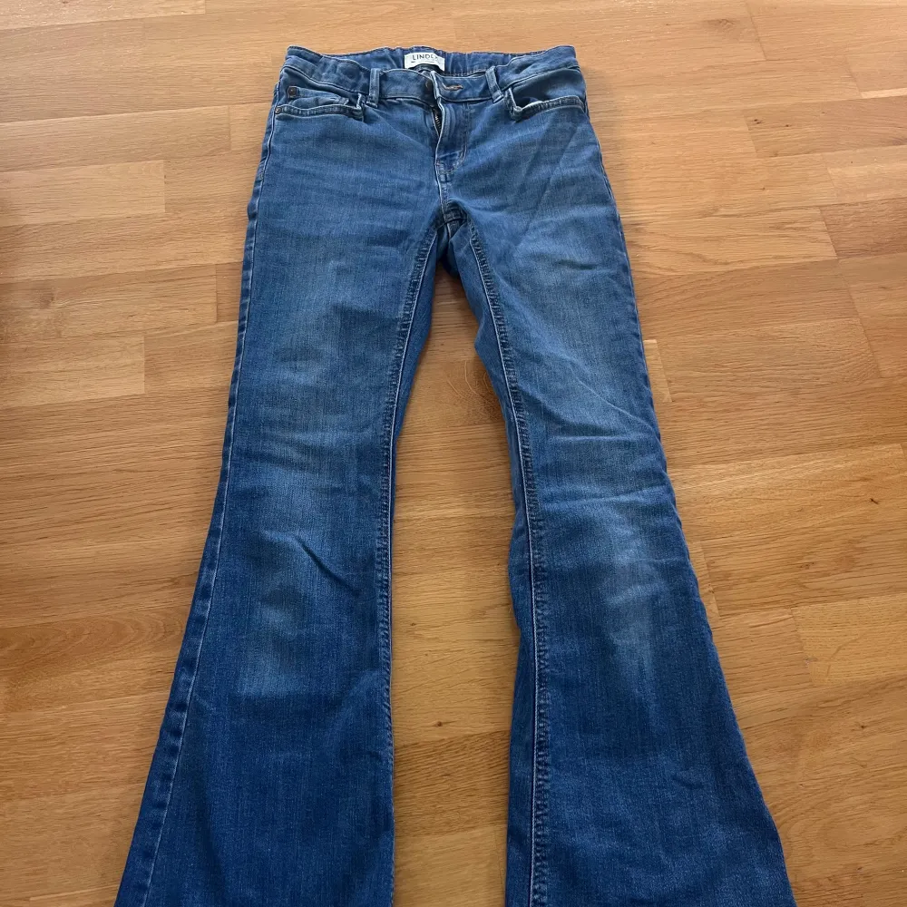 Säljer ett par snygga blå bootcut jeans från Lindex i storlek 158. De är i bra skick och har en klassisk femficksdesign med dragkedja och knapp framtill.  . Jeans & Byxor.