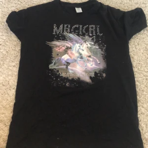 Svart t-shirt med enhörning från Lindex - Säljer en svart t-shirt från Lindex med en magisk enhörning på framsidan. Texten 'MAGICAL' står ovanför enhörningen i glittriga bokstäver. T-shirten är i bra skick och perfekt för alla som älskar enhörningar och magi! 🌟Det är en perfekt tröja till vardagen eller som pyjamas tröja! 