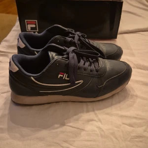 Svarta sneakers från Fila - Säljer ett par svarta sneakers från Fila i modellen Orbit Low. Skorna är i storlek 43 och har en klassisk design med snörning. De är tillverkade i skinn och har en bekväm passform. Perfekta för vardagsbruk eller träning.