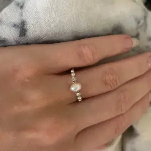 Säljer en superfin ring med en vacker pärla i mitten och små gnistrande stenar på sidorna. Ringen är i guld och har en elegant och tidlös design. Perfekt för både vardag och fest! 💍✨Nyskick aldrig använd, passar mig på pekfinger långfinger och ringfinger