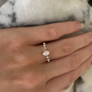 Elegant ring med pärla och stenar - Säljer en superfin ring med en vacker pärla i mitten och små gnistrande stenar på sidorna. Ringen är i guld och har en elegant och tidlös design. Perfekt för både vardag och fest! 💍✨Nyskick aldrig använd, passar mig på pekfinger långfinger och ringfinger