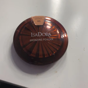 Terracotta Bronze Bronzing Powder från IsaDora - Säljer en bronzer från IsaDora i färgen Terracotta Bronze (43). Den kommer i en snygg, rund förpackning med ett solstrålemönster på locket. Perfekt för att ge ansiktet en solkysst look!