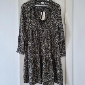 Blommig klänning från Jacqueline de Yong - Säljer en superfin blommig klänning från Jacqueline de Yong. Den är mörkblå, nästintill svart med små blommor i gult och vitt. Den är v-ringad med krage och knäppning vid ärmarna! Aldrig använd dock har min hund tuggat på etiketten men kan klippa bort den vid köp 😅 Materialet är polyster 97%.