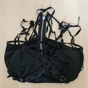 Svart crop top med dragkedja och snörning - Säljer en svart crop top med dragkedja och snörning. Den har en edgy och cool stil med många remmar och detaljer. Perfekt för fest eller en utekväll. Den är i bra skick och har en tight passform. är ett hexagram med snörningen