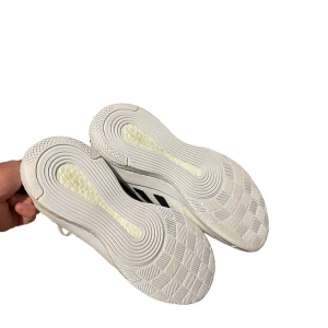 Vita Adidas sneakers med svarta ränder - Säljer ett par vita Adidas sneakers med svarta ränder på sidan. Skorna är i bra skick och har en modern design med snörning. Perfekta för både vardag och träning. De är bekväma och stilrena, passar till många olika outfits.