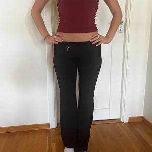 Svarta byxor med hög midja och gulddetalj - Säljer ett par svarta mjukisbyxor med låg midja och en snygg gulddetalj på midjebandet. Byxorna är i ett stretchigt och bekvämt material. De har en tight passform upptill och blir vidare nedtill, vilket ger en smickrande siluett. 