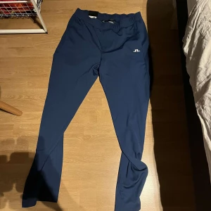 Blå byxor från J. Lindeberg - Snygga blå byxor från J. Lindeberg, modell Clive Pants. Perfekta för en stilren look med en bekväm passform. Byxorna har en elastisk midja och är i en djup blå färg. Ny pris 1000kr (aldrig använda)